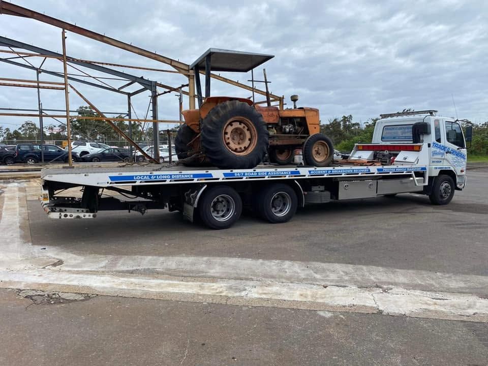 White flatbed tow truck carrying an orange tractor