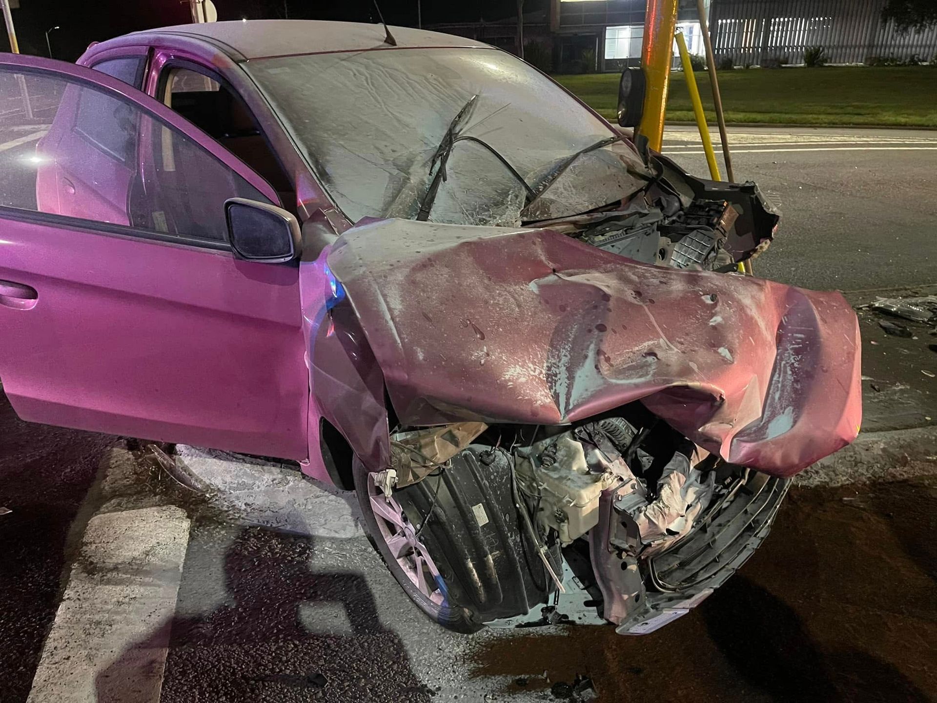 Severely damaged pink car with crumpled front end at night