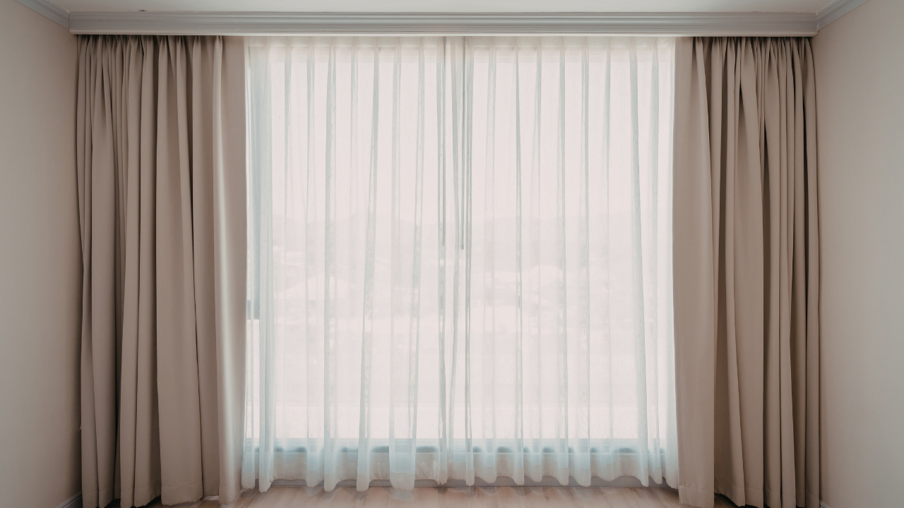 Floor-to-ceiling beige curtains framing sheer white drapes over a large window