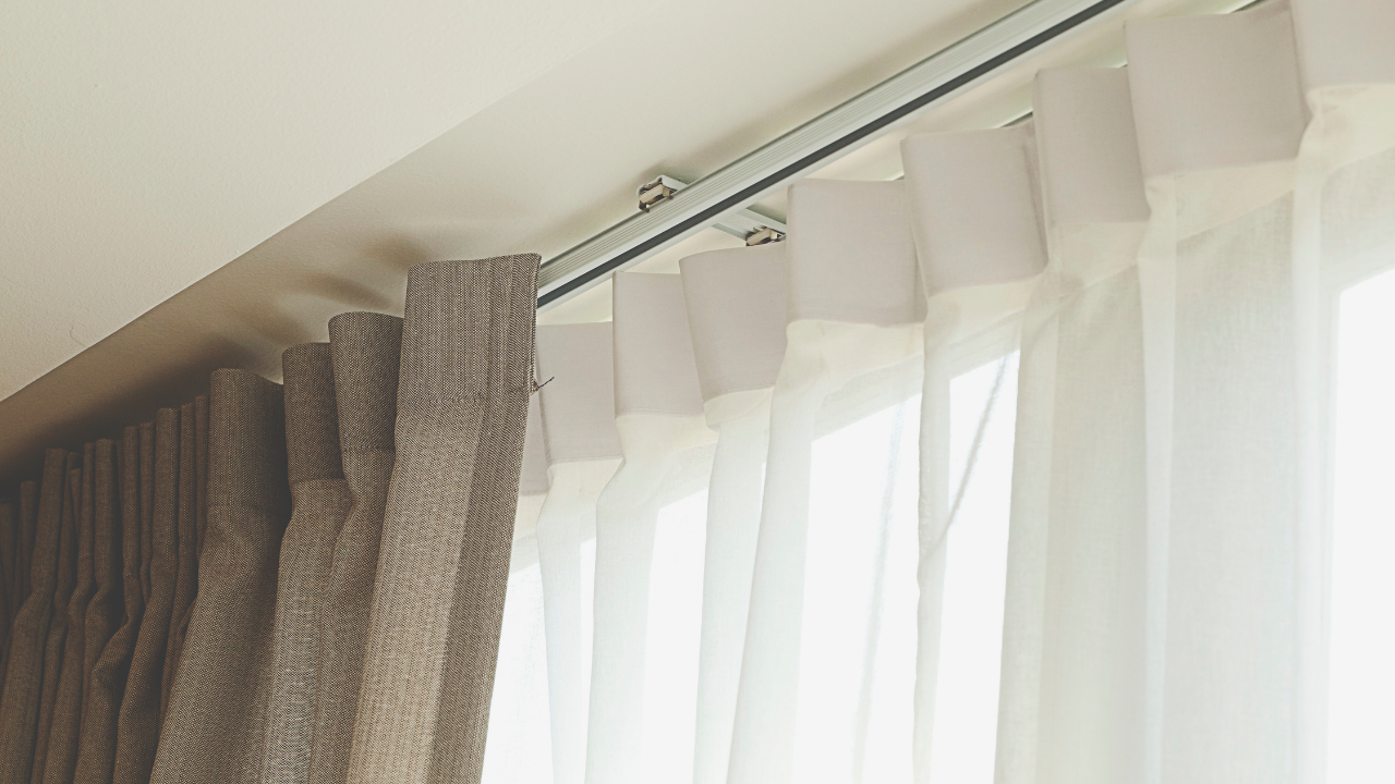 Sheer white curtains beside beige drapes on a curtain rod near a slanted ceiling