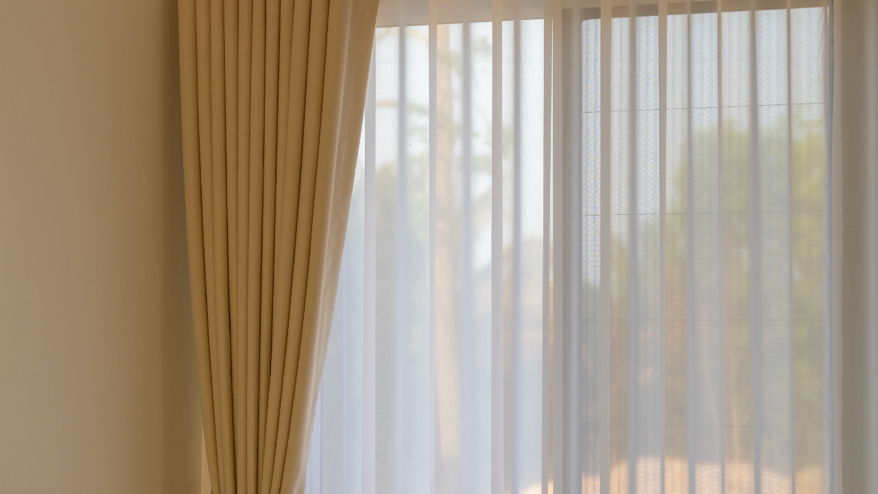 Sheer white curtains and beige drapes over a sunlit window