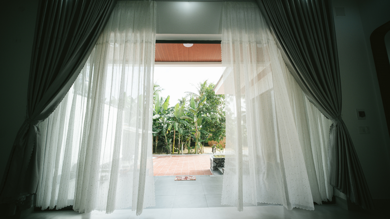 Curtains framing a bright window opening to a sunny garden patio outside