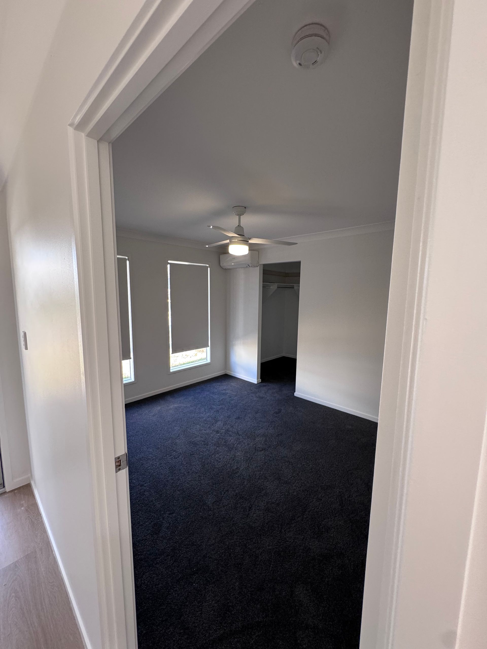 Empty carpeted room with white walls, ceiling fan, and doorway view