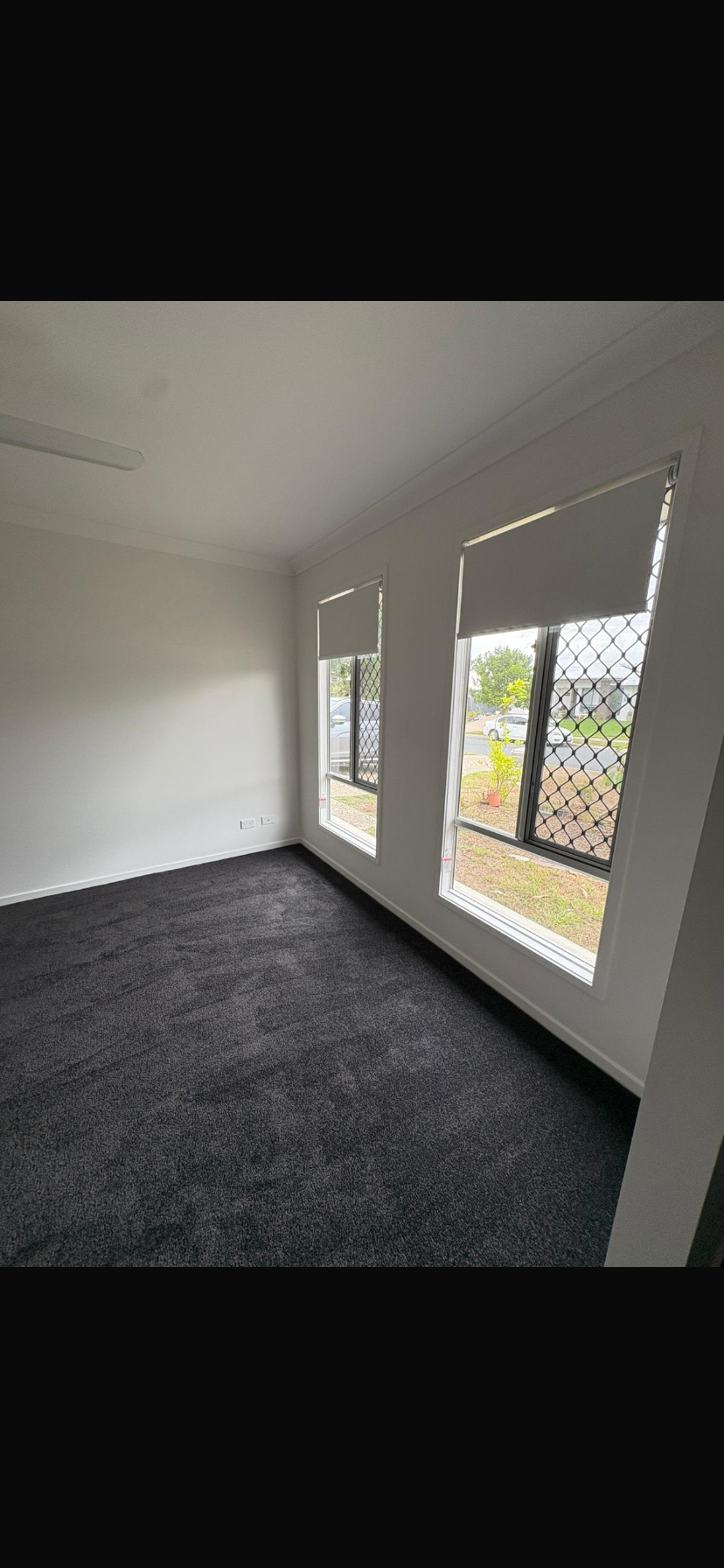 Empty room with gray carpet, white walls, and large windows overlooking trees and grass.