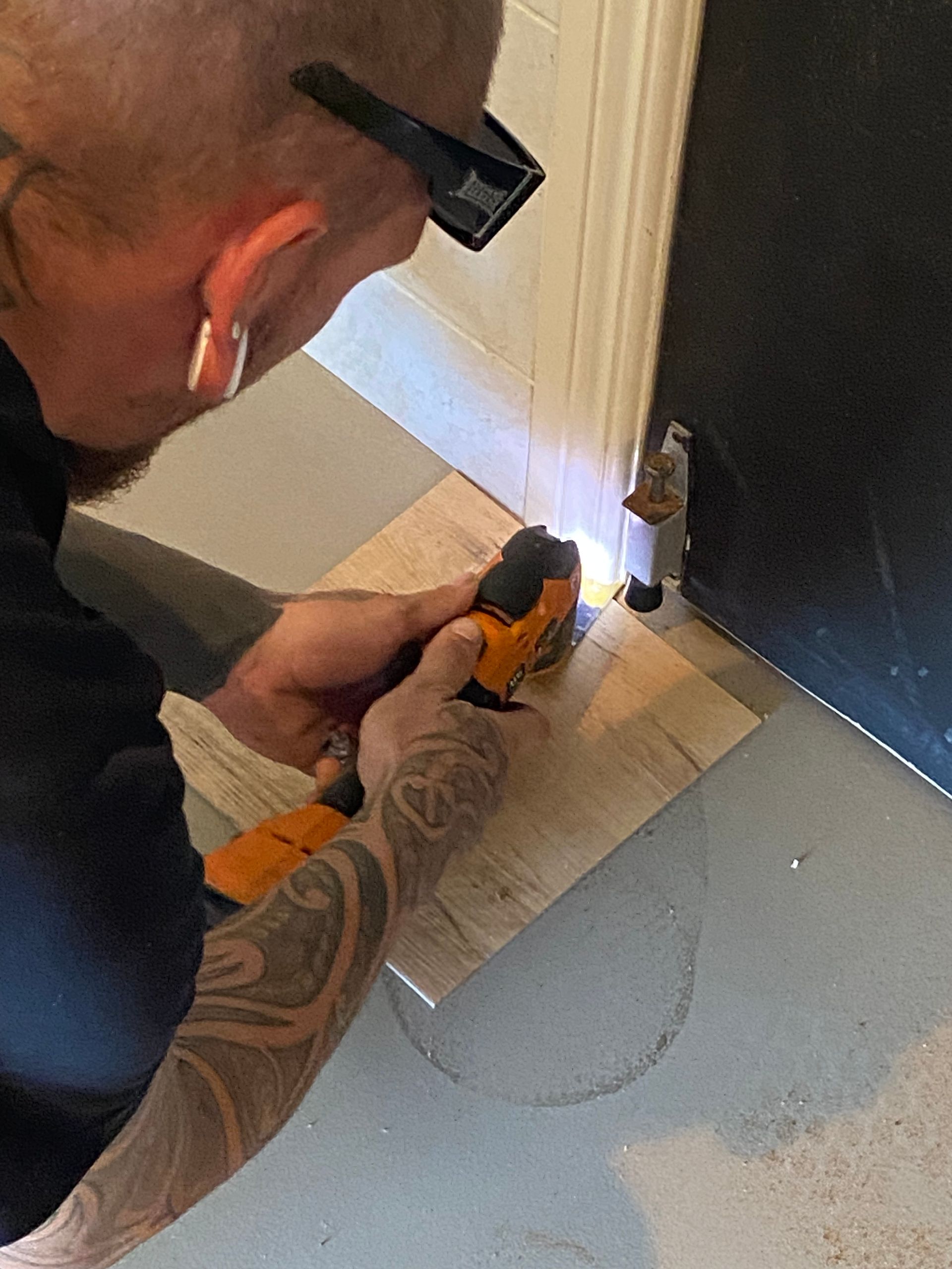 Person using an orange power tool to work on a door frame near the floor.