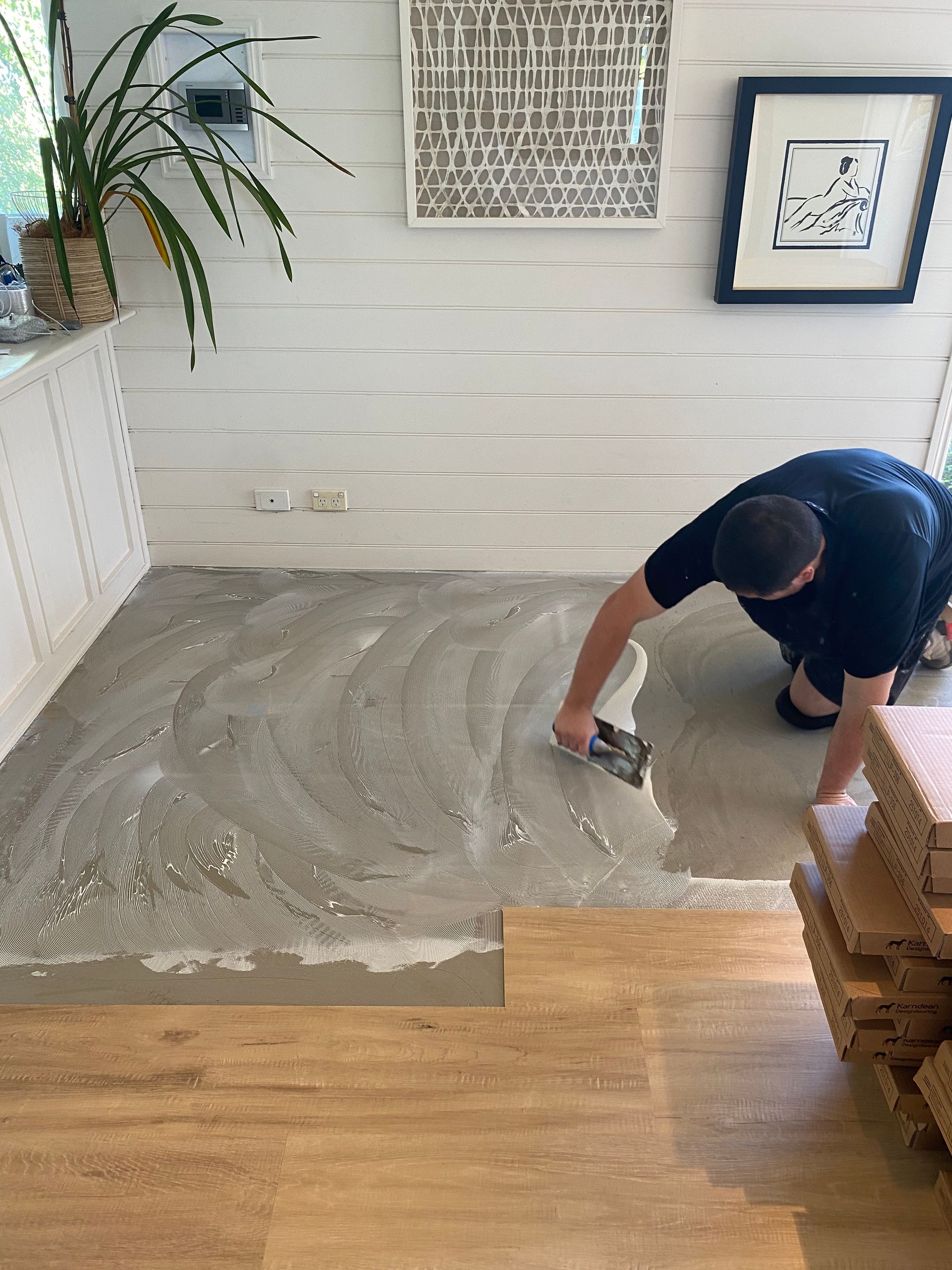 Person smoothing wet concrete on a floor beside a wood floor in a bright room
