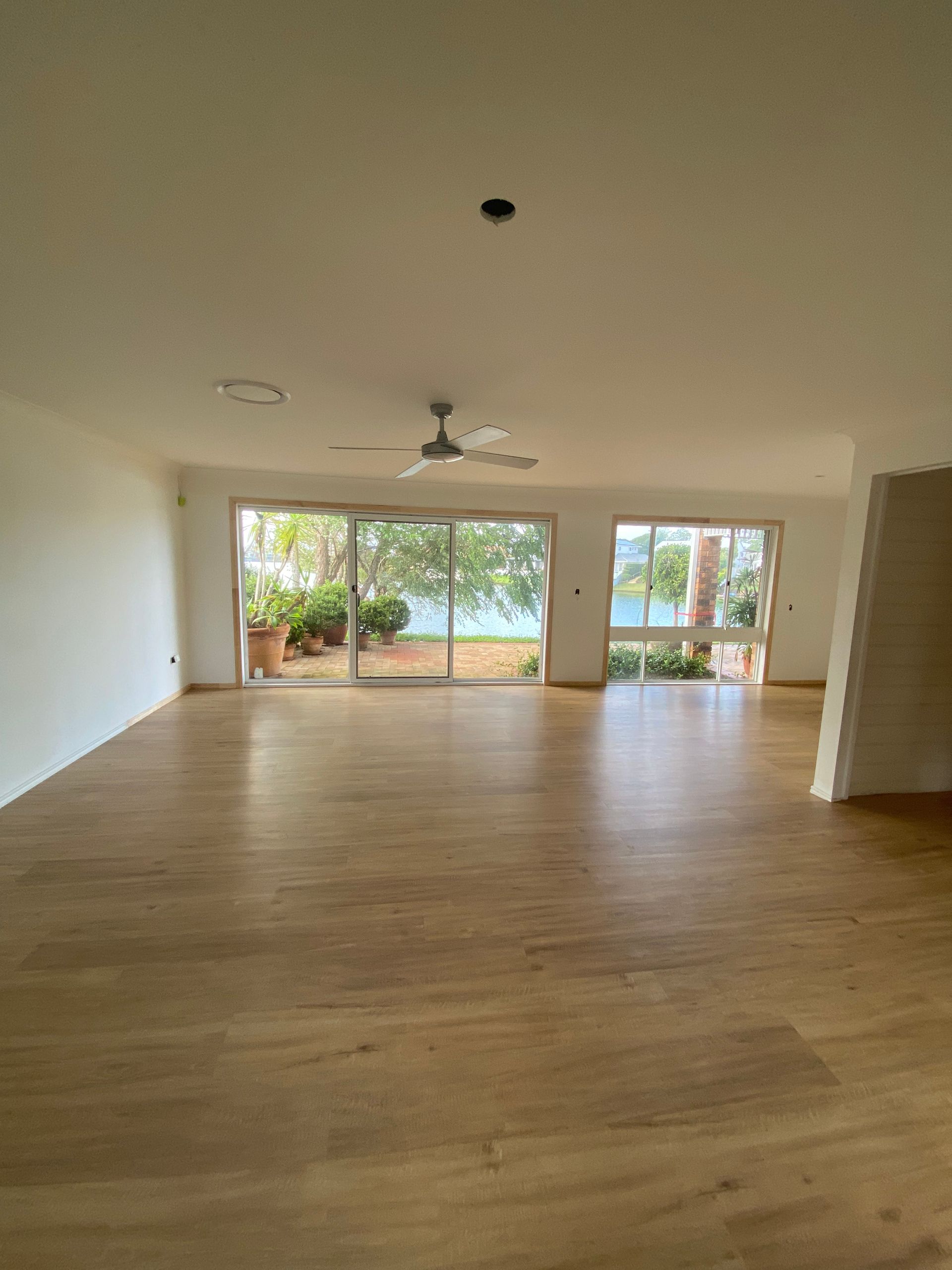 Empty living room with wood floors, ceiling fan, and large sliding glass doors opening to a green yard