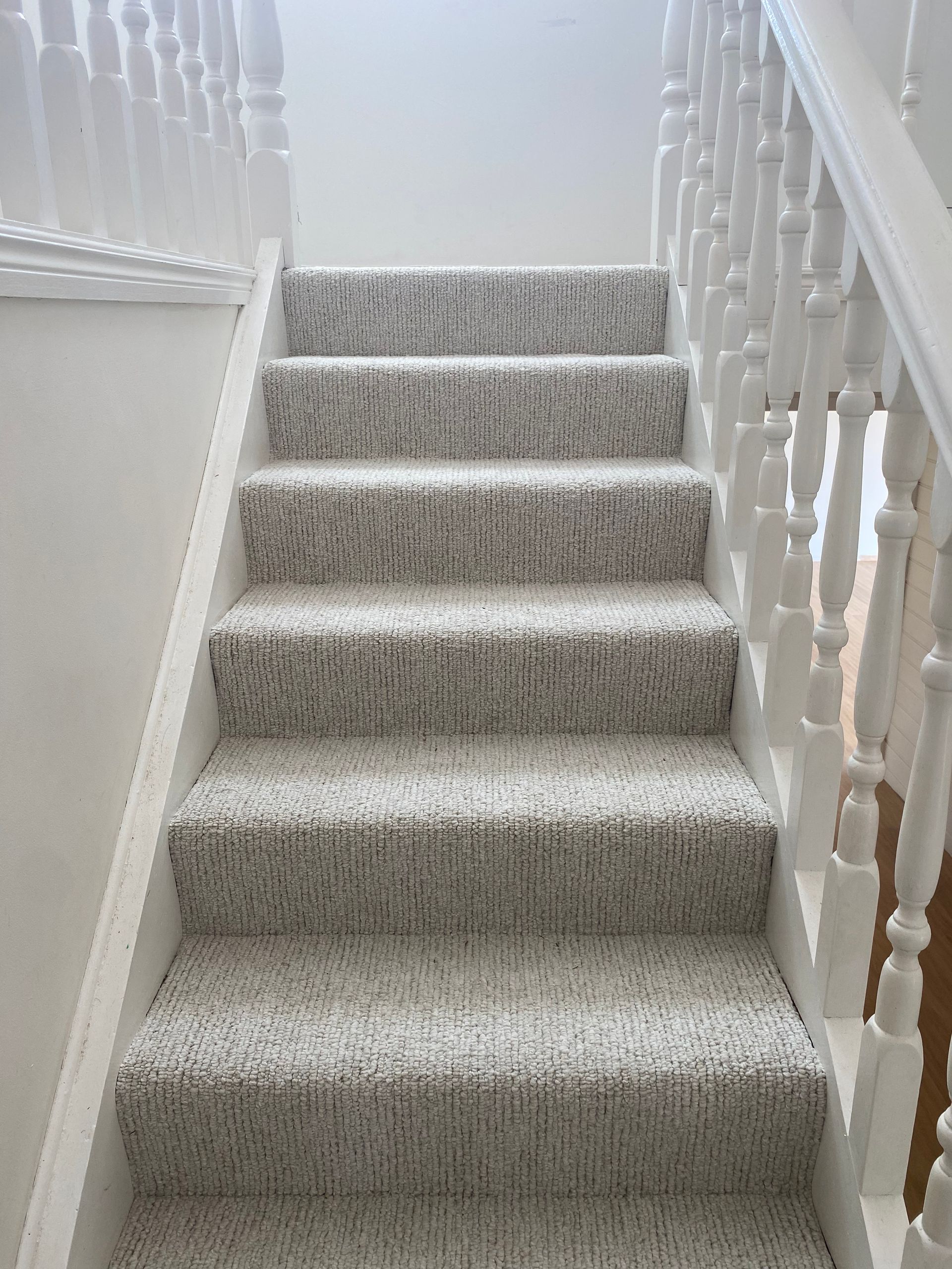 Carpeted indoor staircase with white banisters and beige walls, viewed from the bottom up.