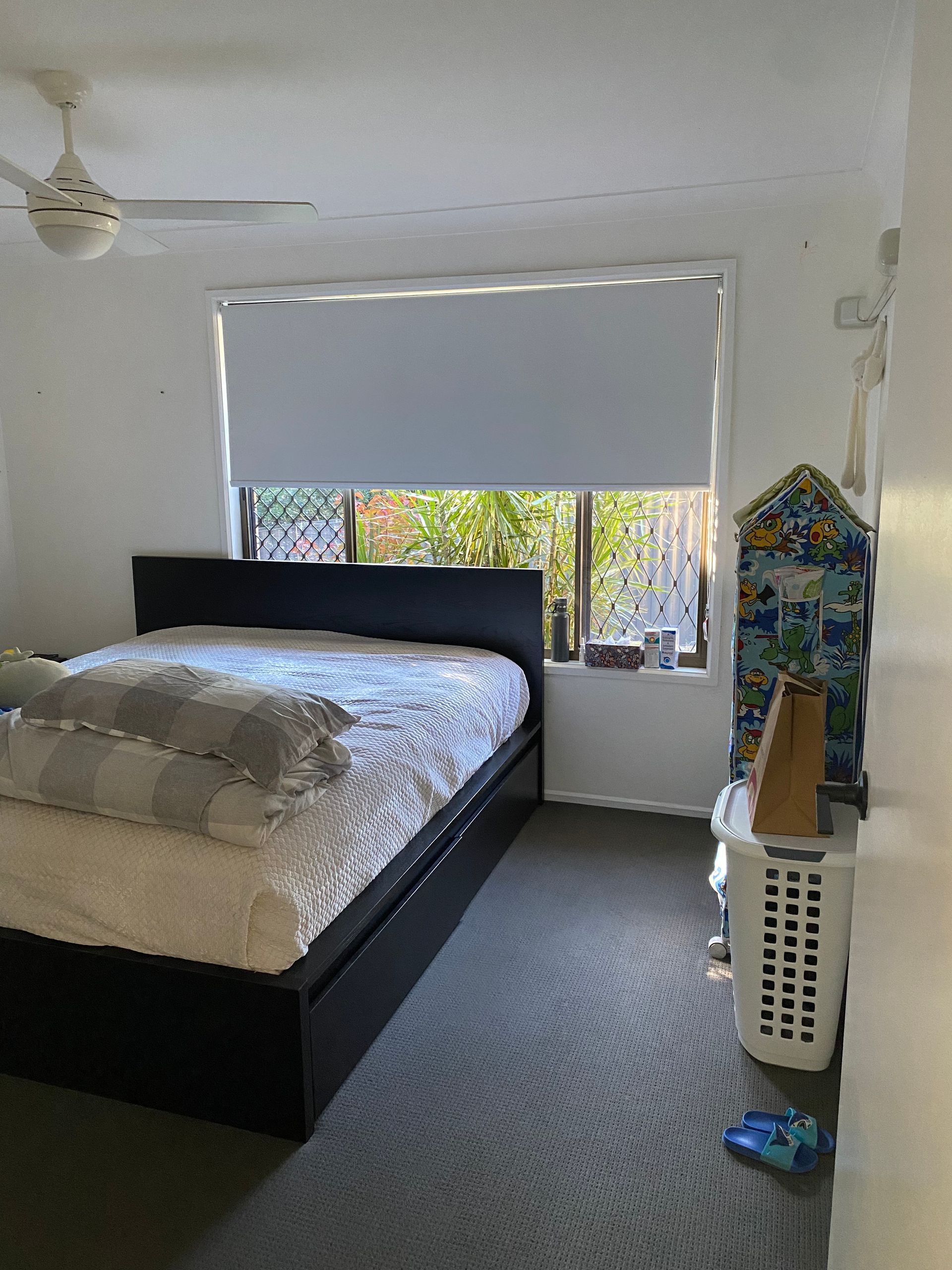 Bedroom with black bed, white walls, bright window, and laundry basket near a small stand
