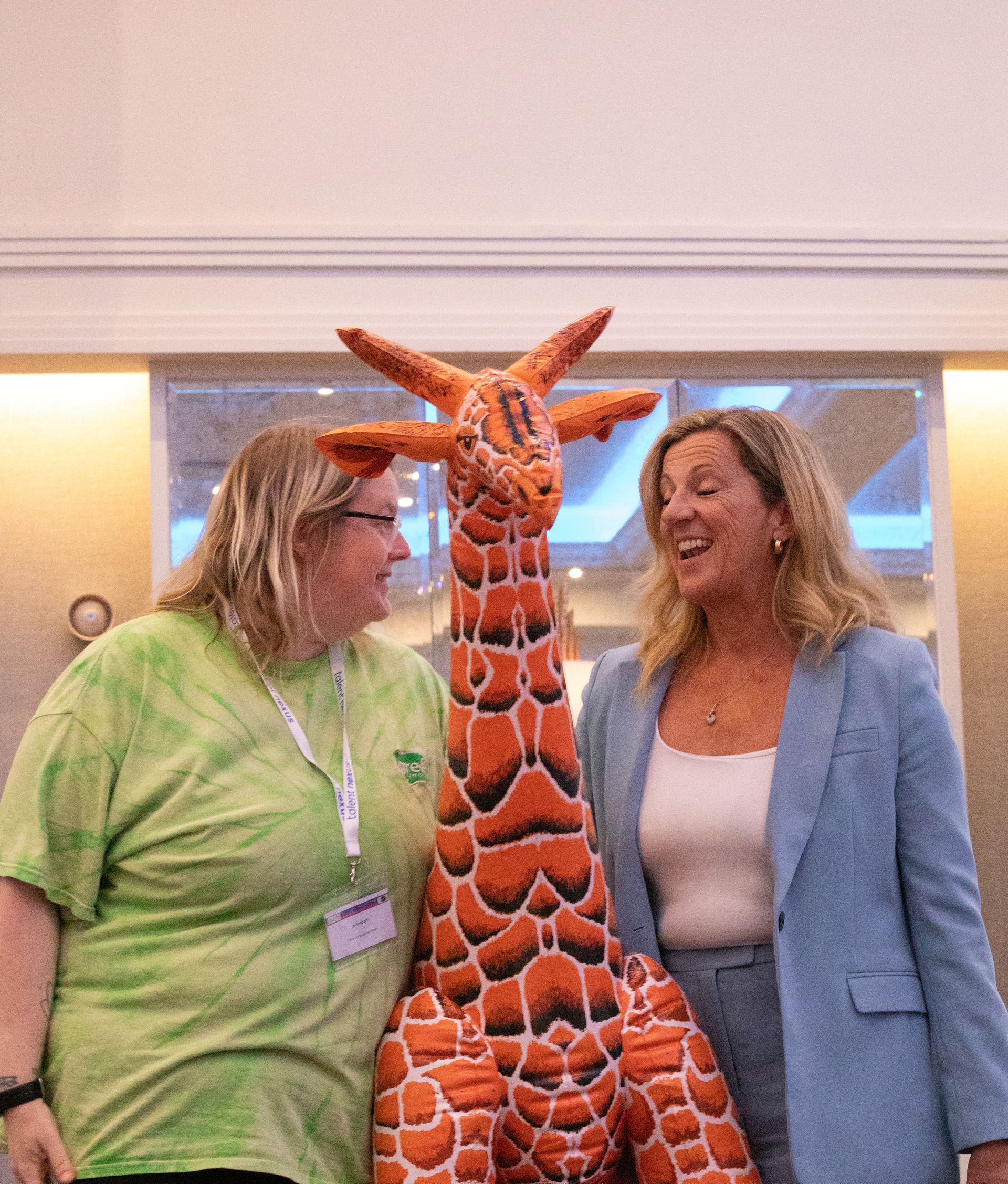 Two women are standing next to a stuffed giraffe.