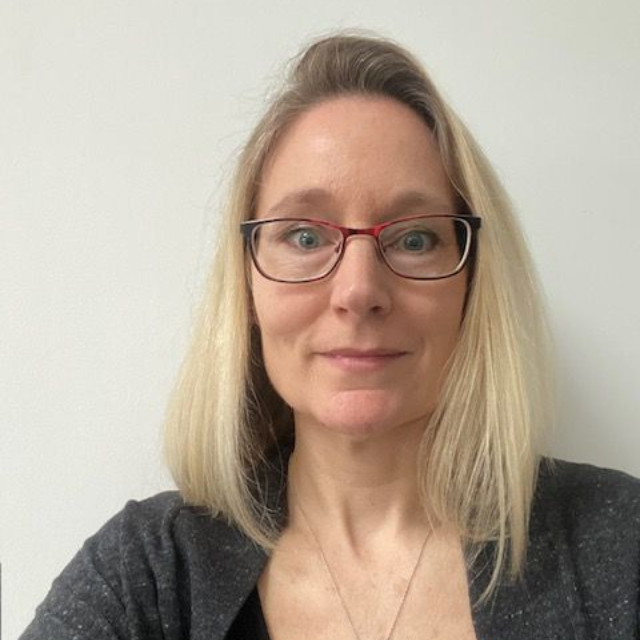 A woman wearing a blazer and earrings is looking at the camera.