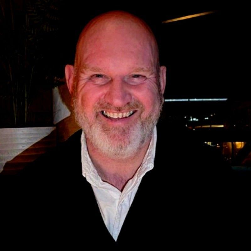 A man in a grey shirt is smiling for the camera
