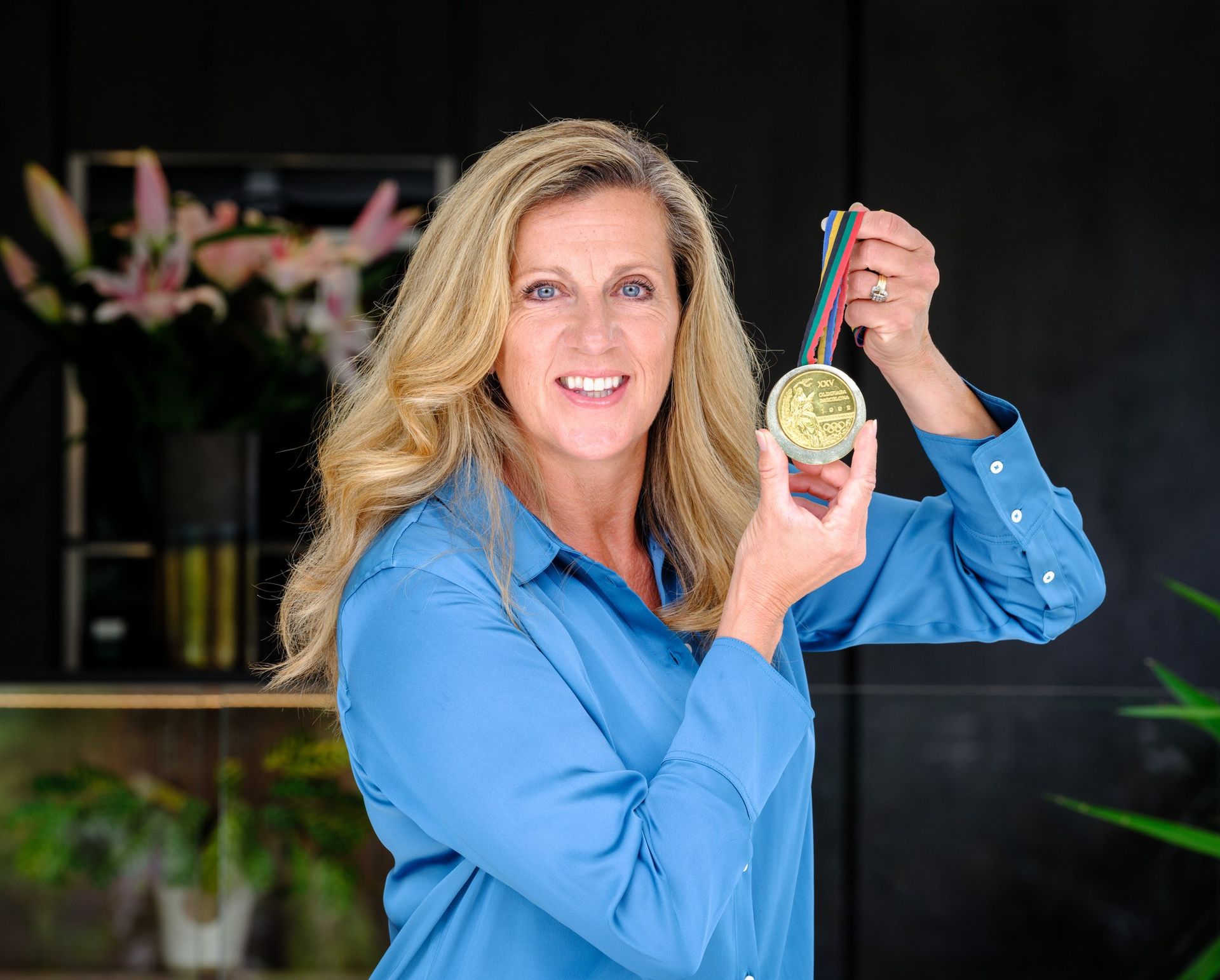 A woman in a blue shirt is holding a gold medal.