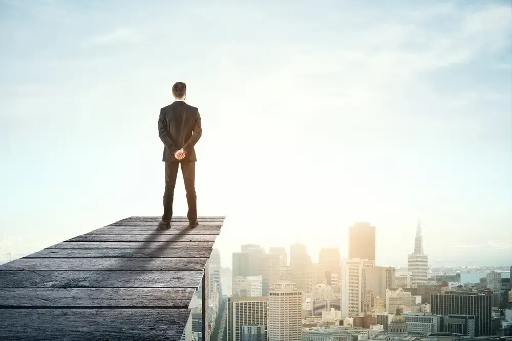 A man in a suit is standing on top of a bridge overlooking a city.