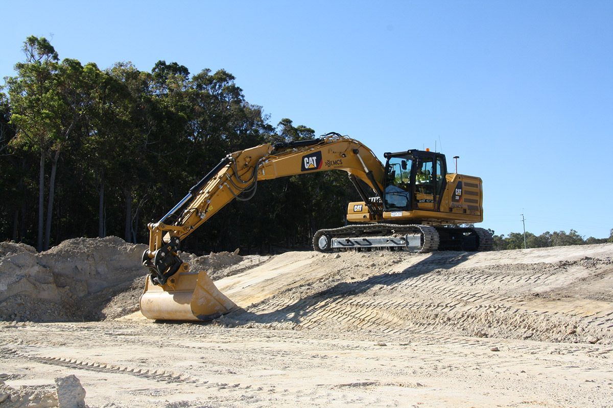A yellow cat excavator is working on a dirt field