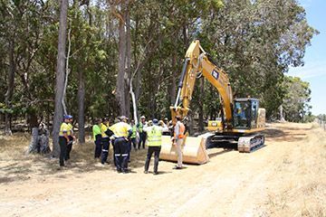 A group of people are standing around an excavator in a field.