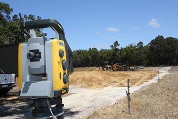 A yellow and gray total station is sitting on the side of a dirt road.