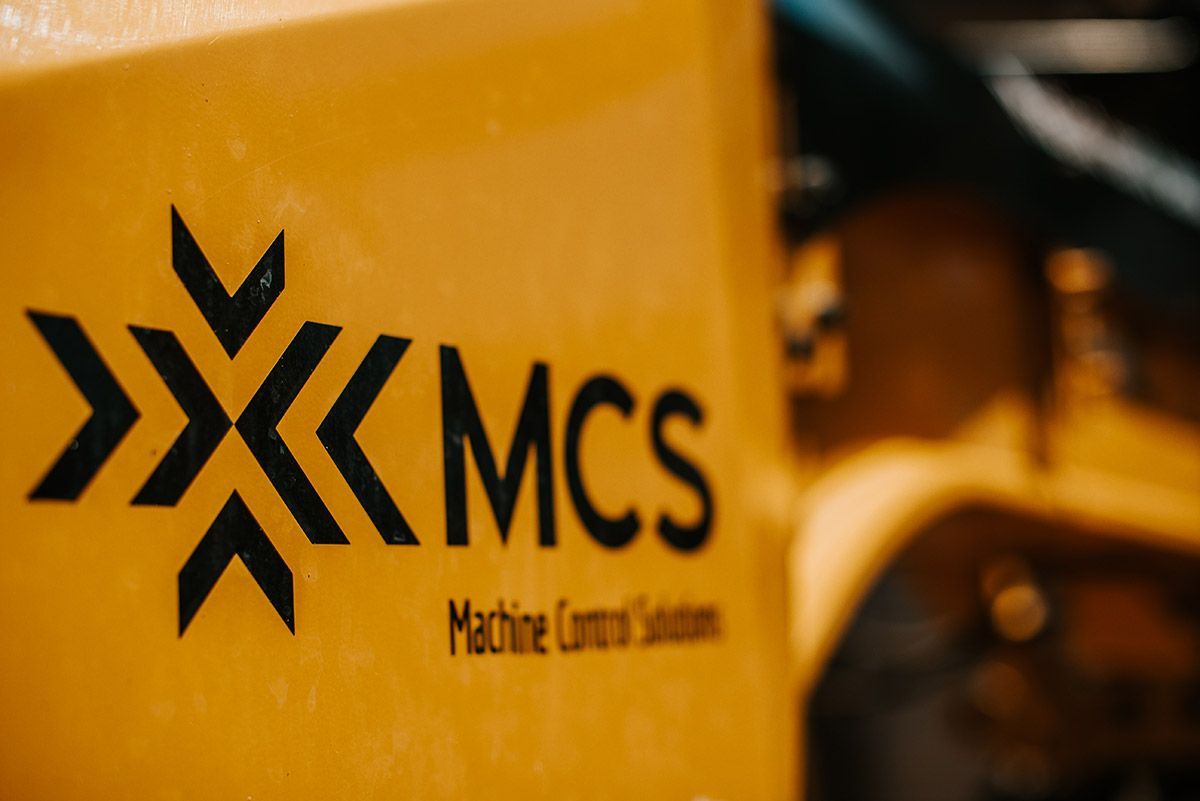 A close up of a mcs machine control solution logo