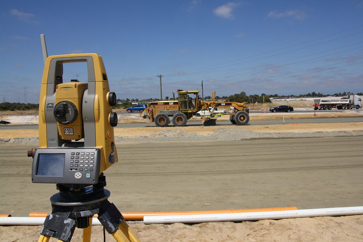 A theodolite is sitting on a tripod on a construction site