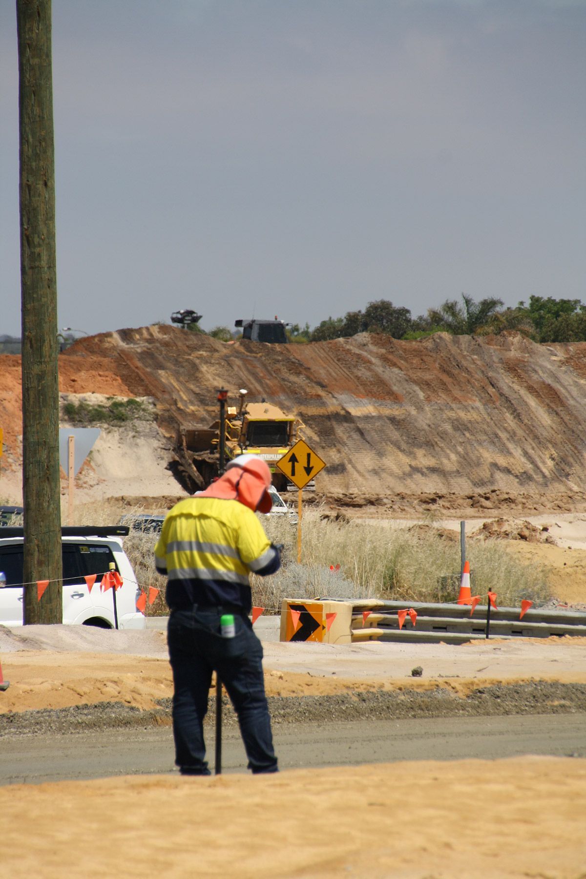 A man wearing headphones and a hard hat is standing in front of a construction site.