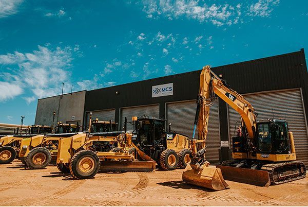 A row of construction vehicles are parked in front of a building.