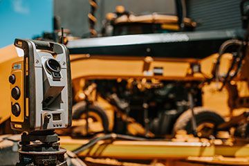 A theodolite is sitting in front of a yellow bulldozer.