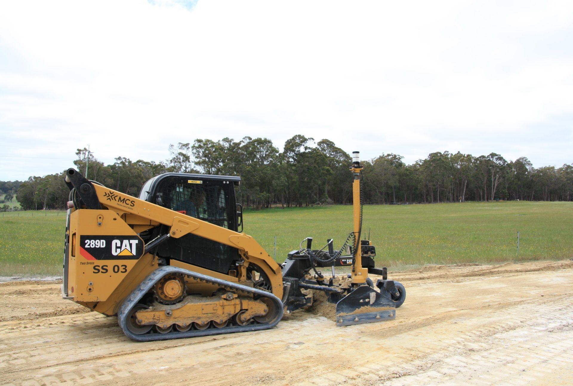 A cat tractor is driving down a dirt road.