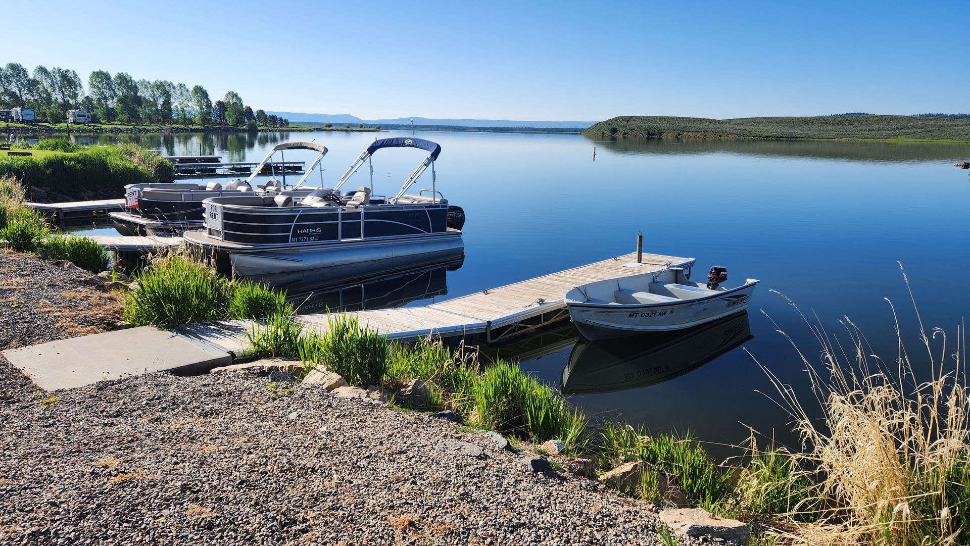 Boats docked on a calm blue lake beside a rocky shore under a clear sky