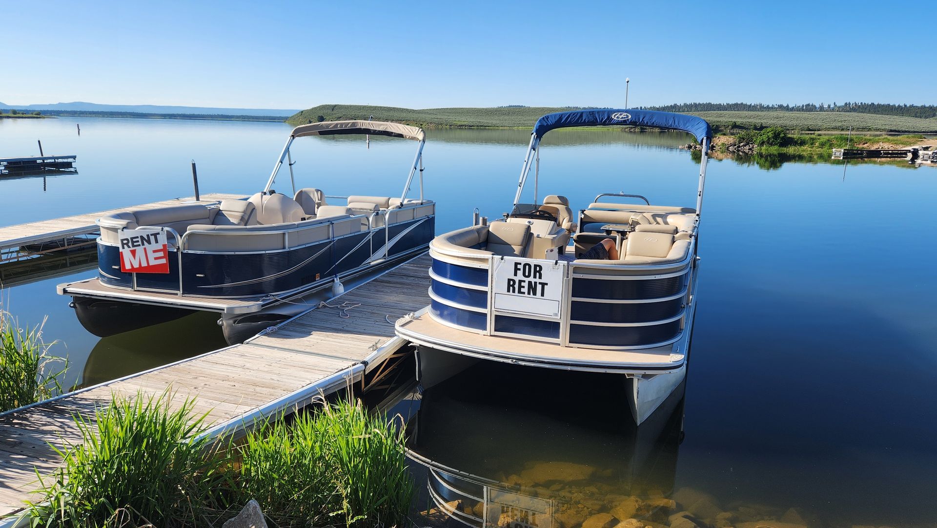 Two pontoon boats docked on a calm lake under a clear blue sky.