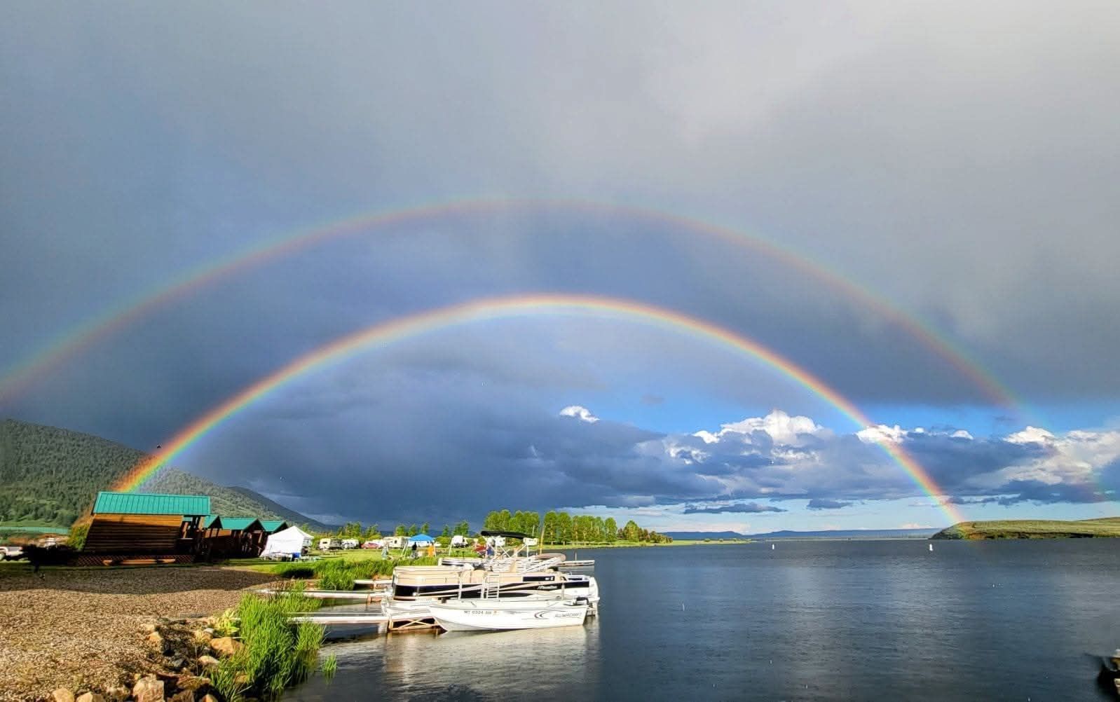 Double rainbow over a calm harbor with boats and a cloudy sky