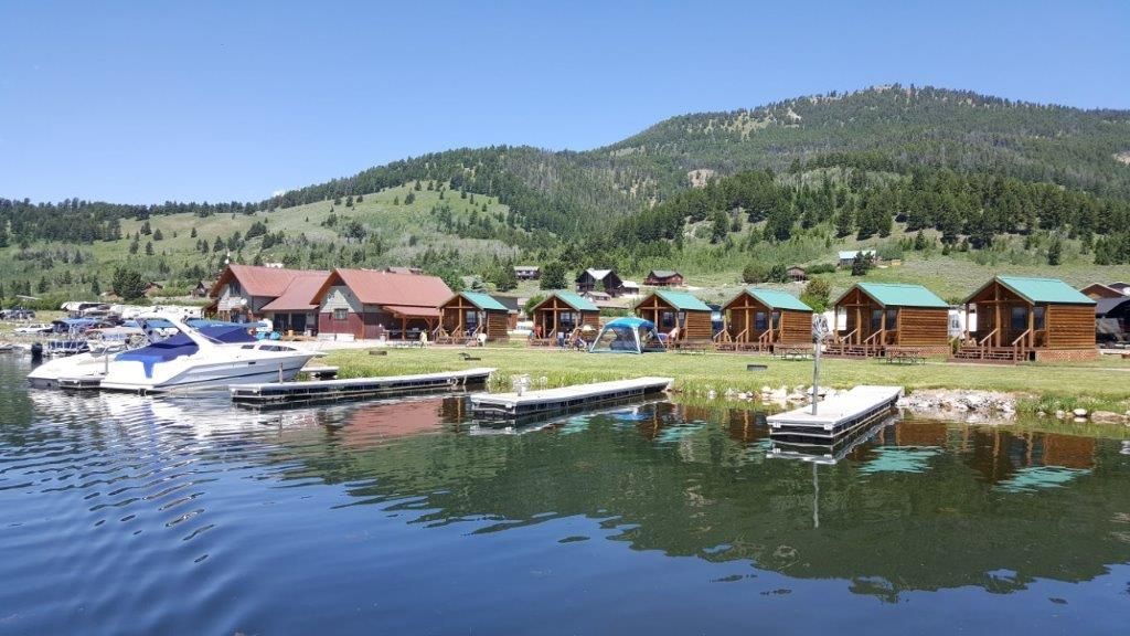 Boats docked on a lake beside cabins and pine-covered hills under a clear sky
