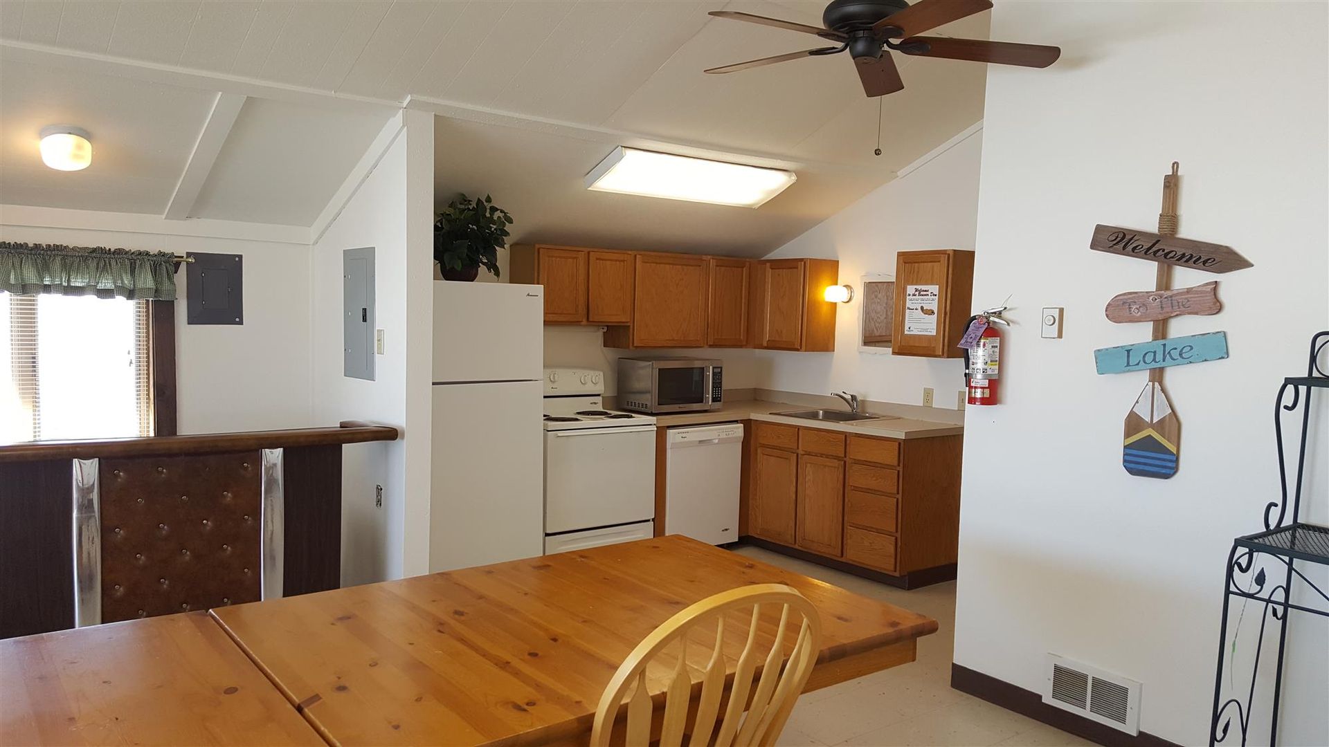 Open kitchen and dining area with wood cabinets, white appliances, ceiling fan, and wooden table and chairs.