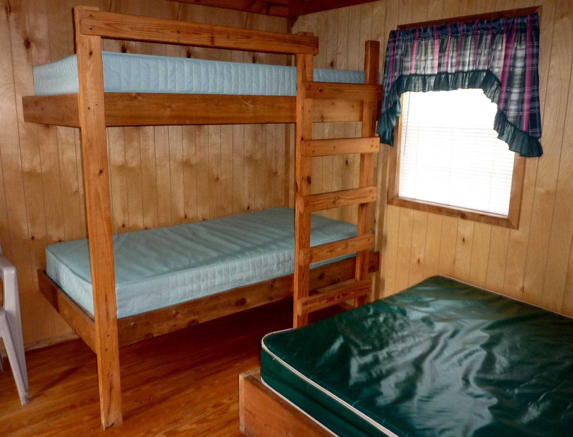 Wood-paneled cabin bedroom with bunk beds, a single bed, and a window with plaid curtains.
