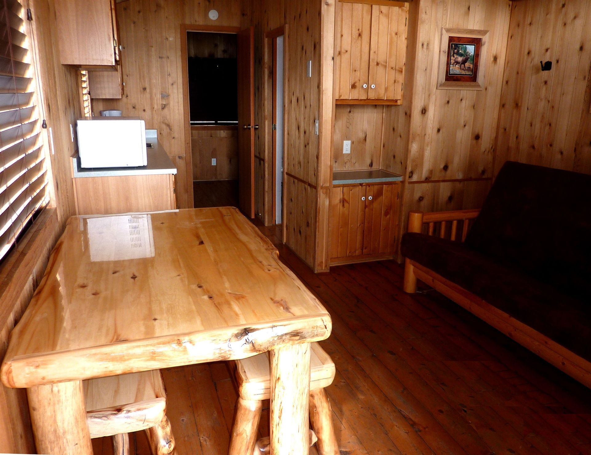 Wood-paneled cabin room with a wooden table, sofa, and small sink by a doorway