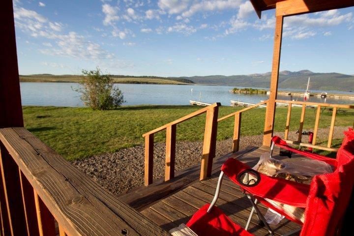 Wooden deck with red chairs overlooking a calm lake and distant hills at sunset