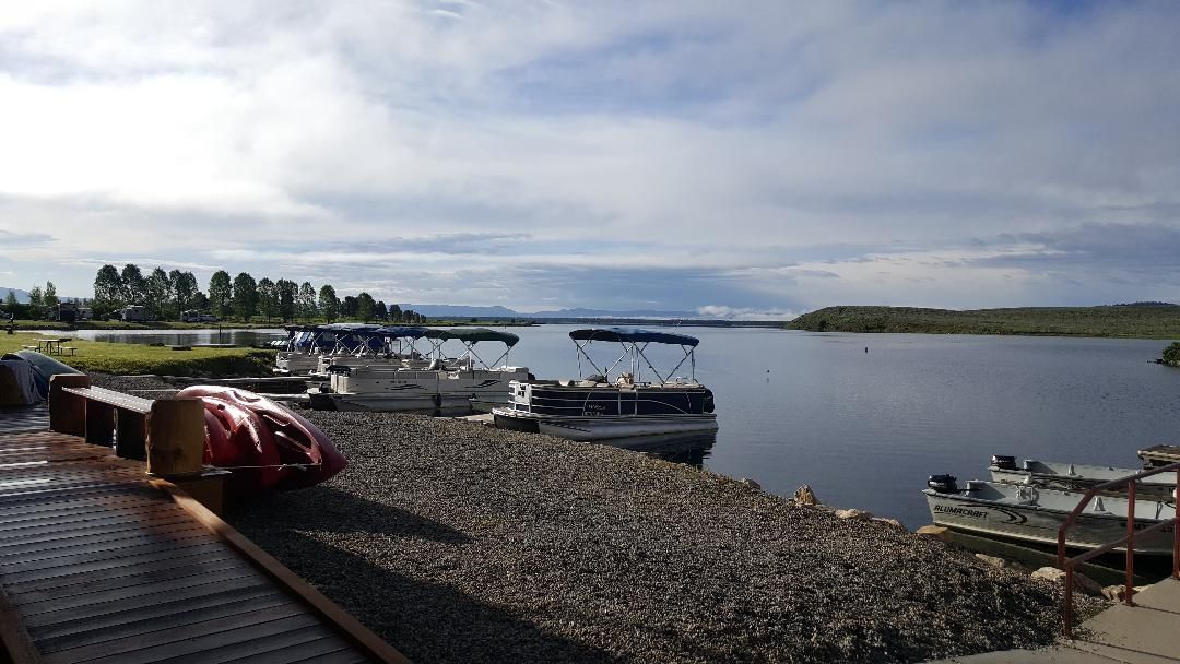 Small boats moored at a rocky waterfront under a cloudy sky, with calm water and distant shoreline.