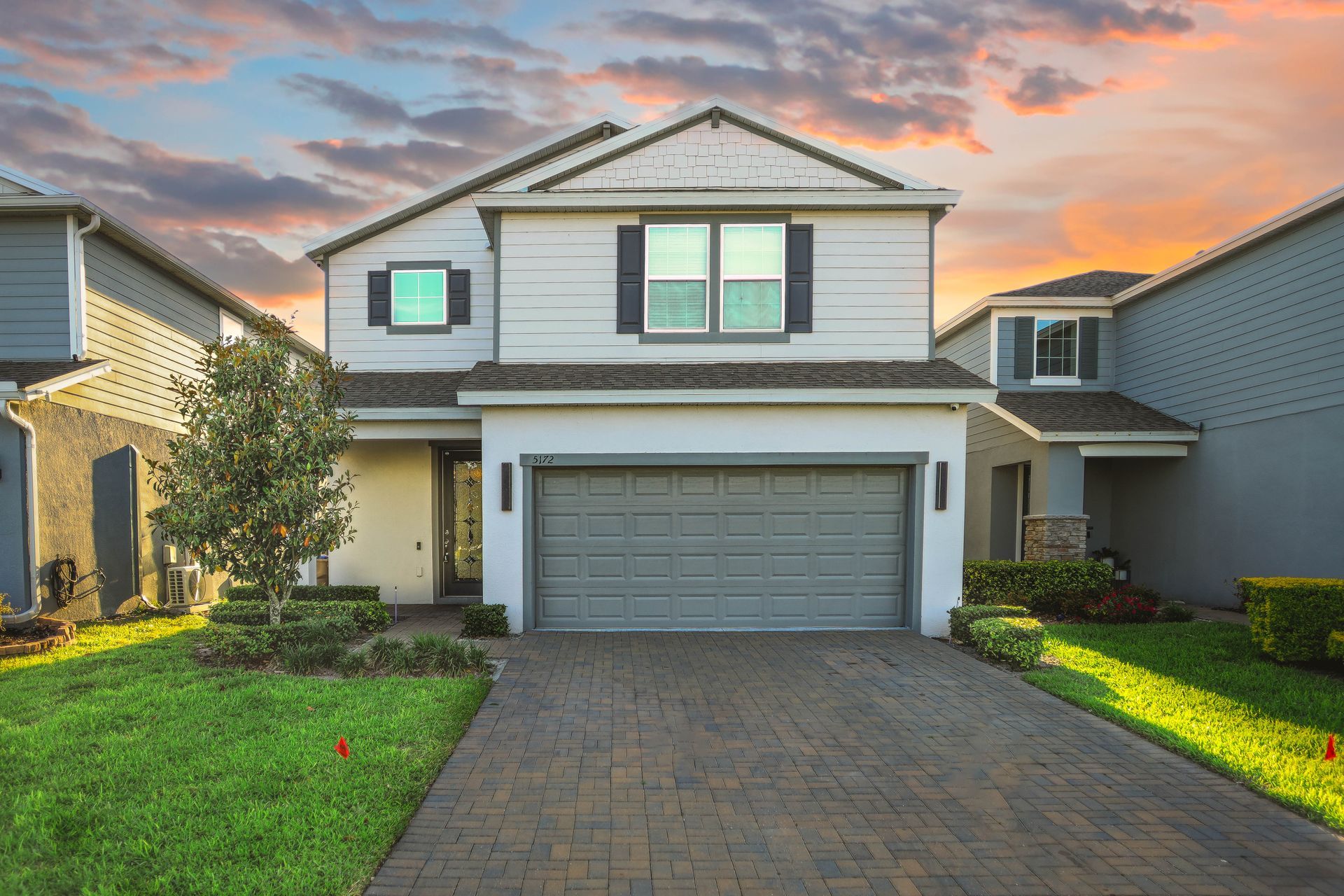 Two-story suburban house with gray garage and brick driveway at sunset