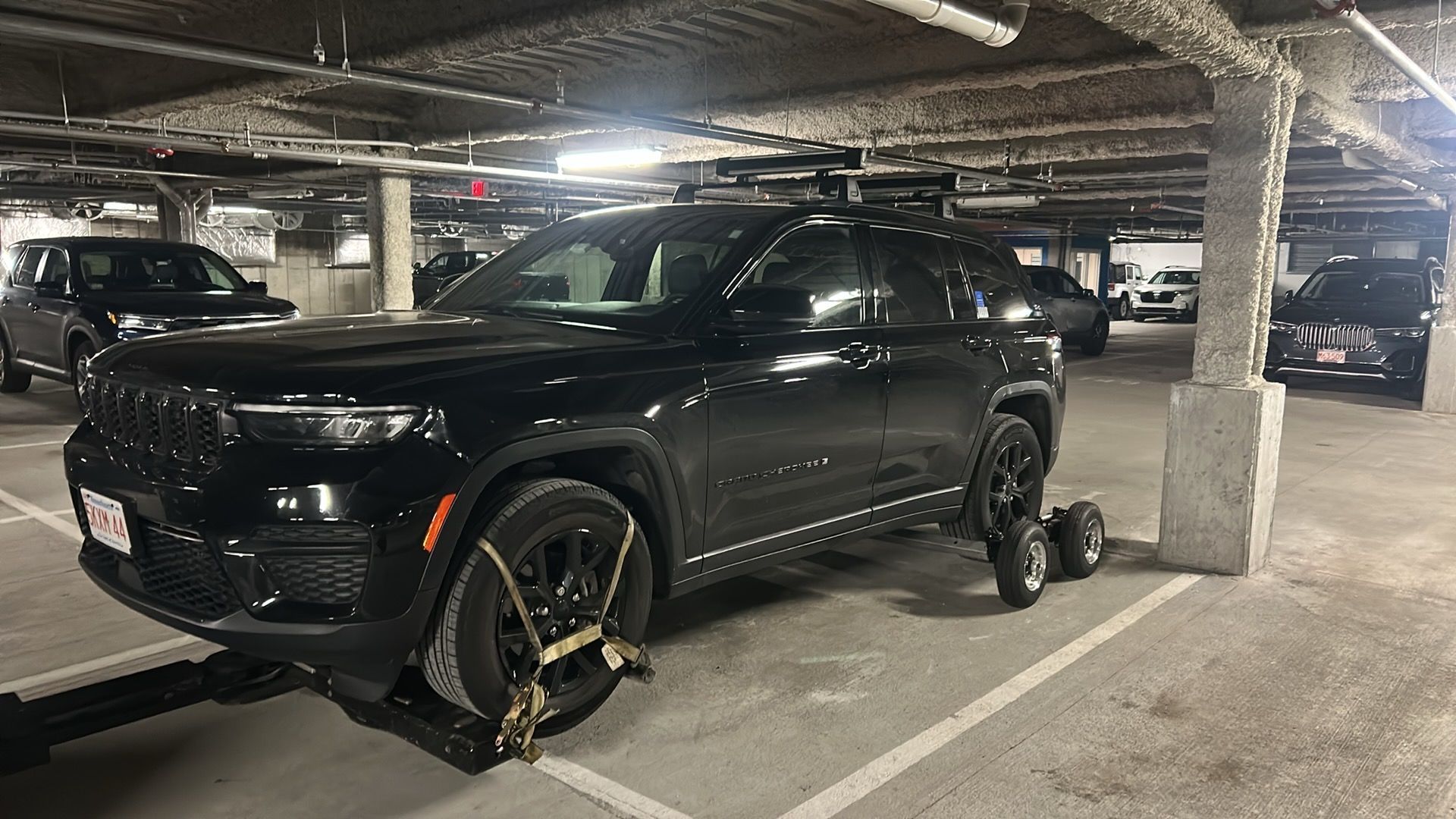 Black SUV parked in an underground garage, with a wheel lock on the front tire.