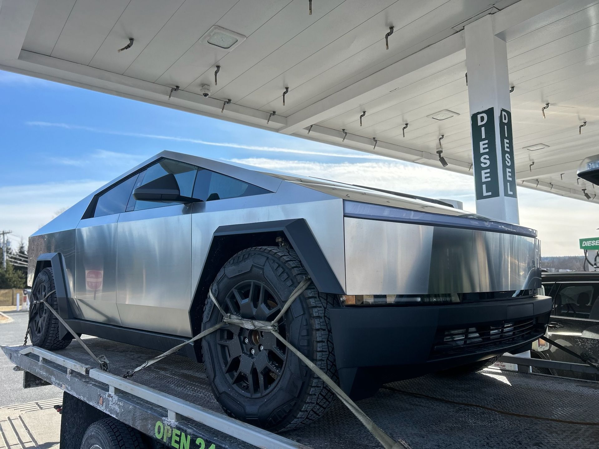 Angular silver Tesla Cybertruck at a charging station under a canopy.