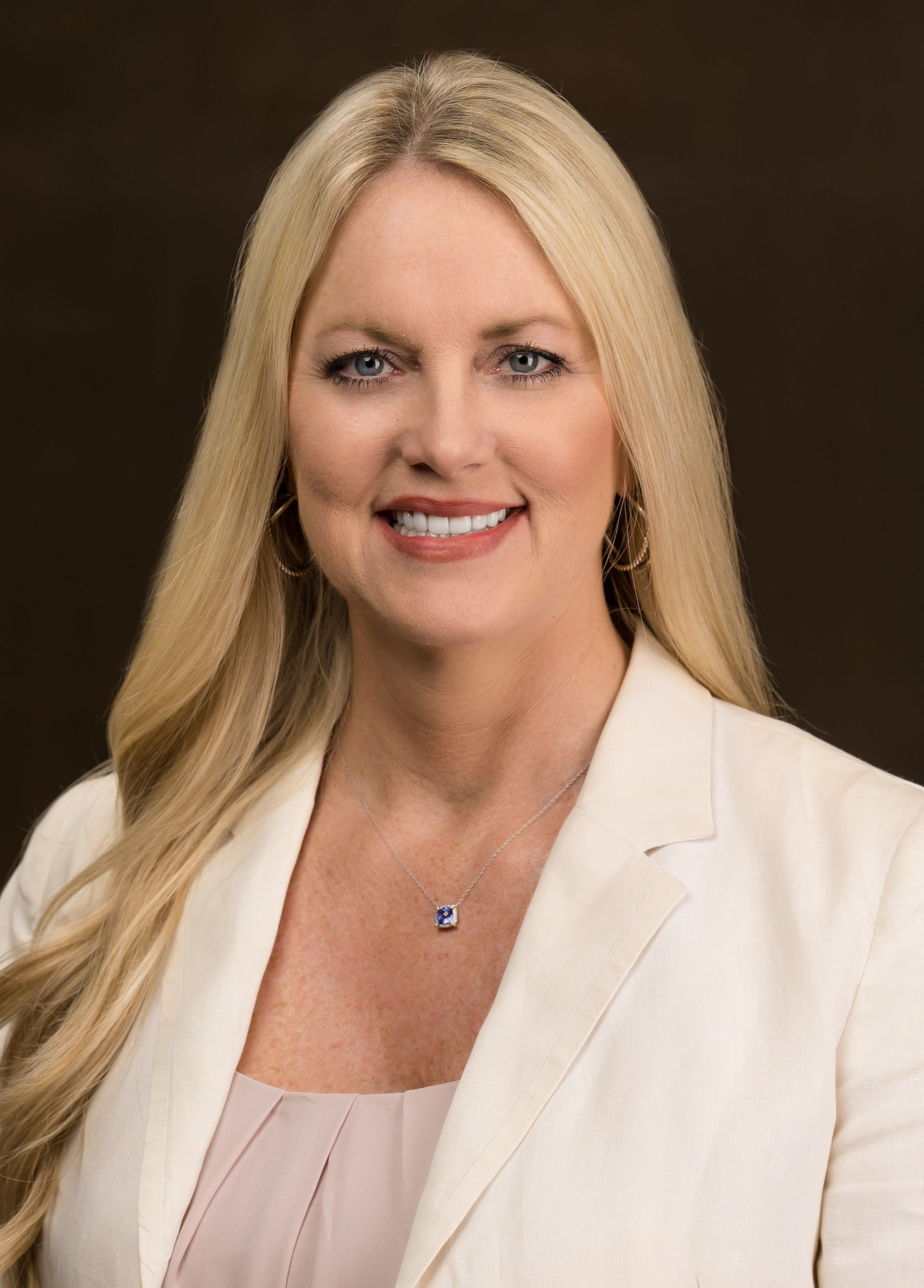 Woman with long blonde hair, wearing a white blazer, smiling at the camera.