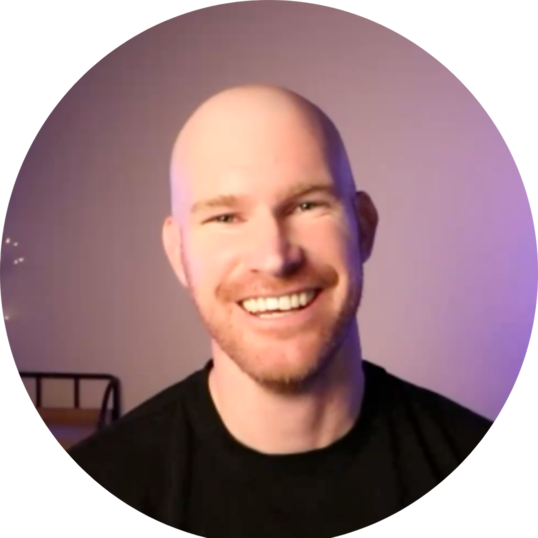 Smiling bald person in a black shirt against a softly lit purple background
