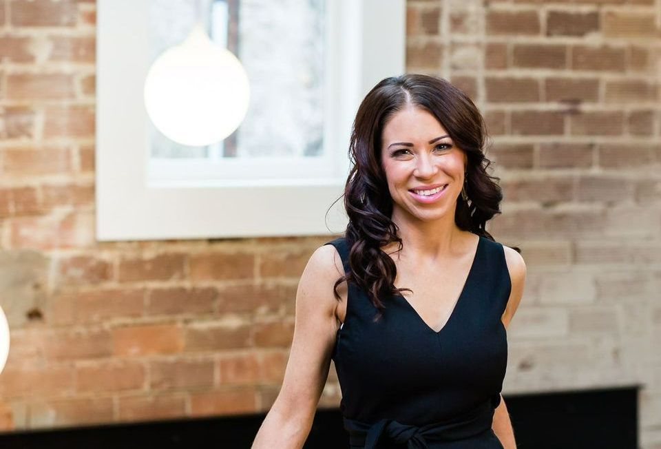 A woman in a black dress is standing in front of a brick wall.