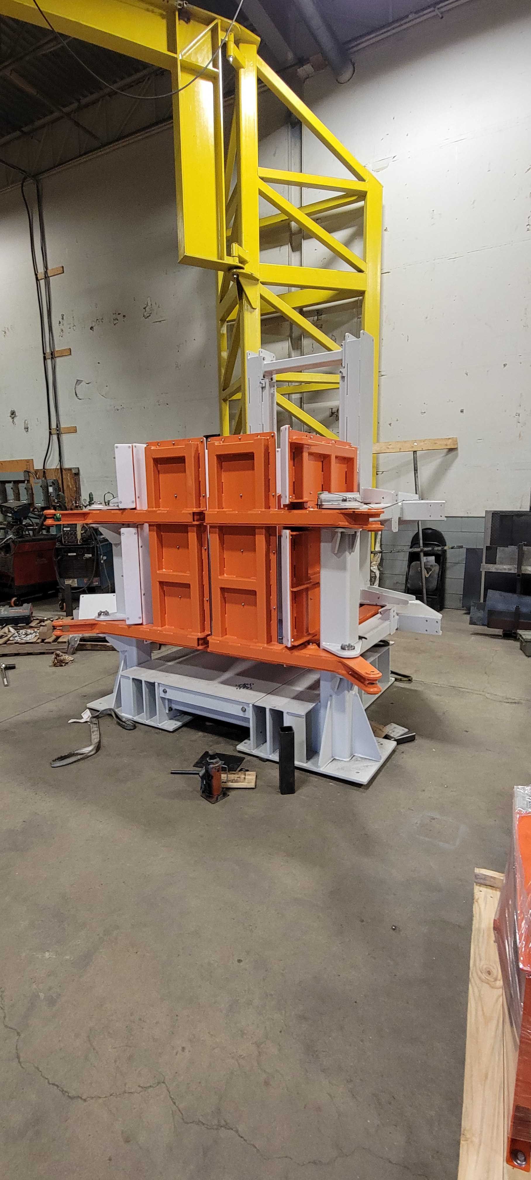 Équipements industriels avec un socle en métal blanc et des blocs modulaires orange dans un entrepôt avec un pont roulant jaune.