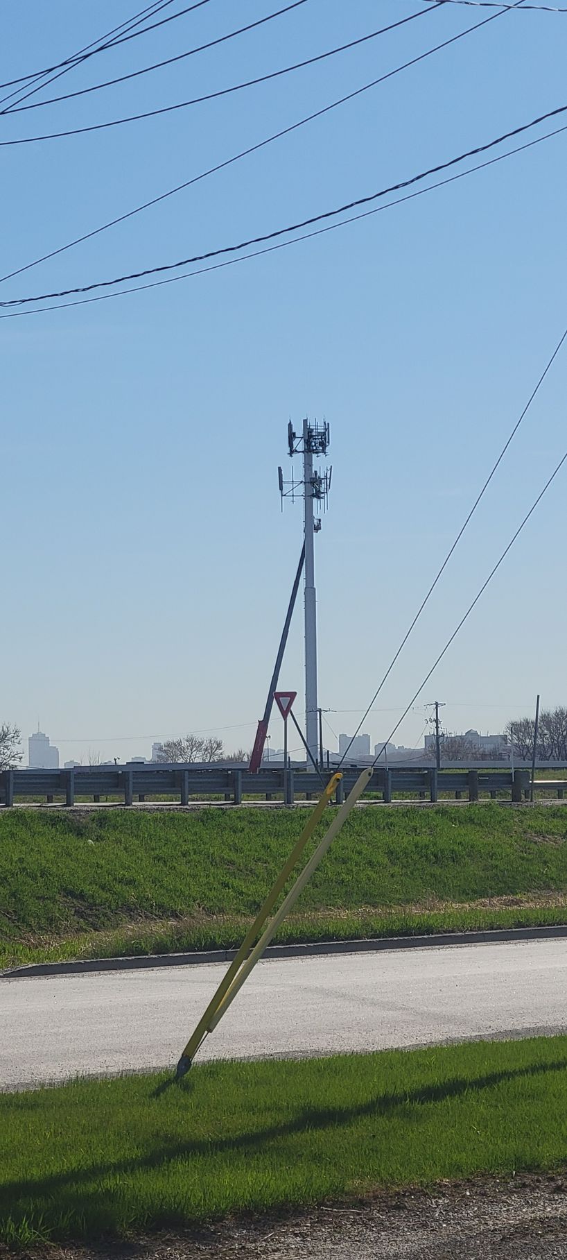 Une antenne-relais de téléphonie mobile se dresse au milieu d'un champ herbeux sous un ciel bleu azur, avec des lignes électriques visibles au premier plan.