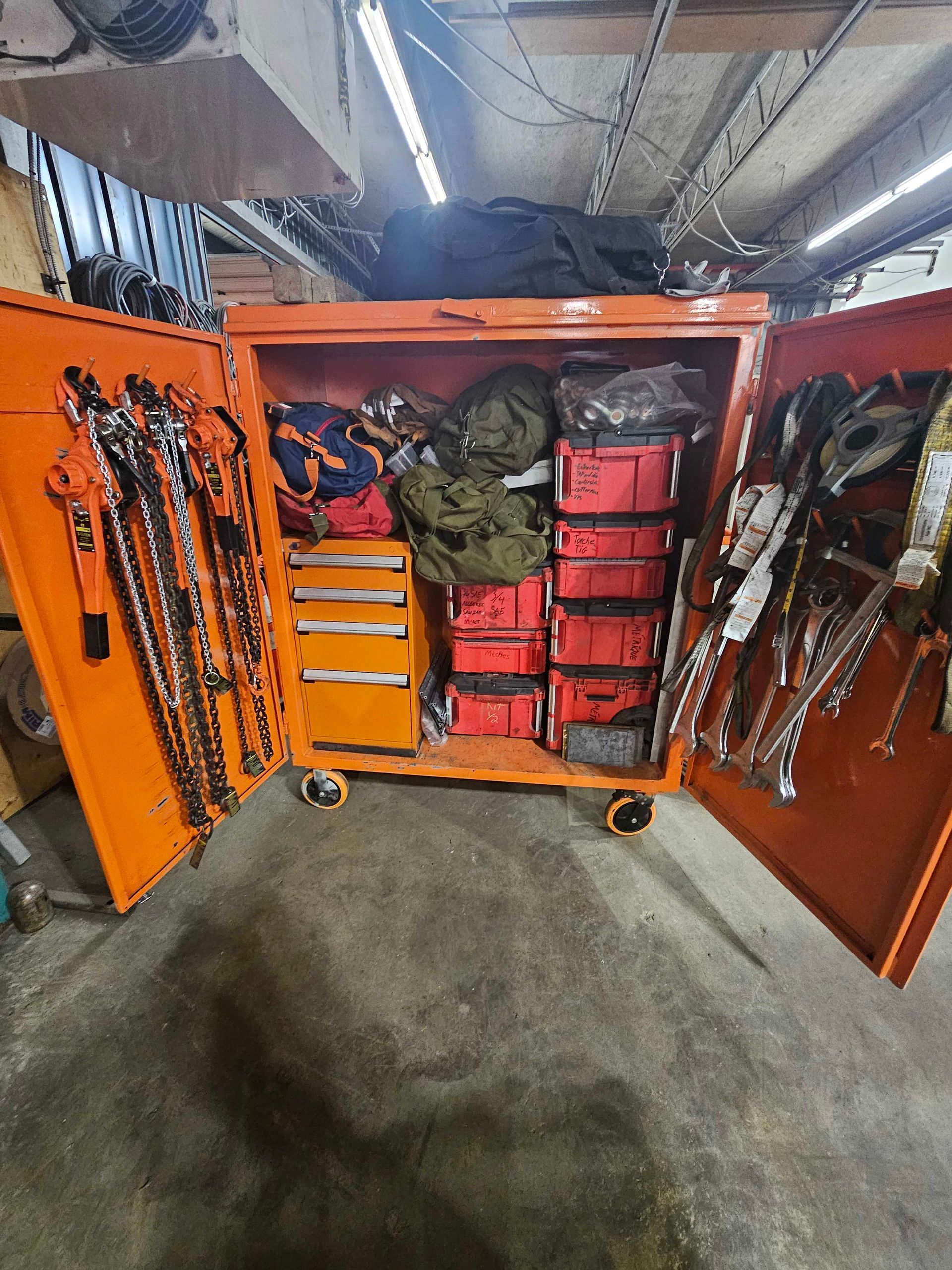 Boîte à outils métallique orange ouverte, remplie de caisses à outils rouges empilées, de tiroirs et de matériel d'escalade accroché aux portes.