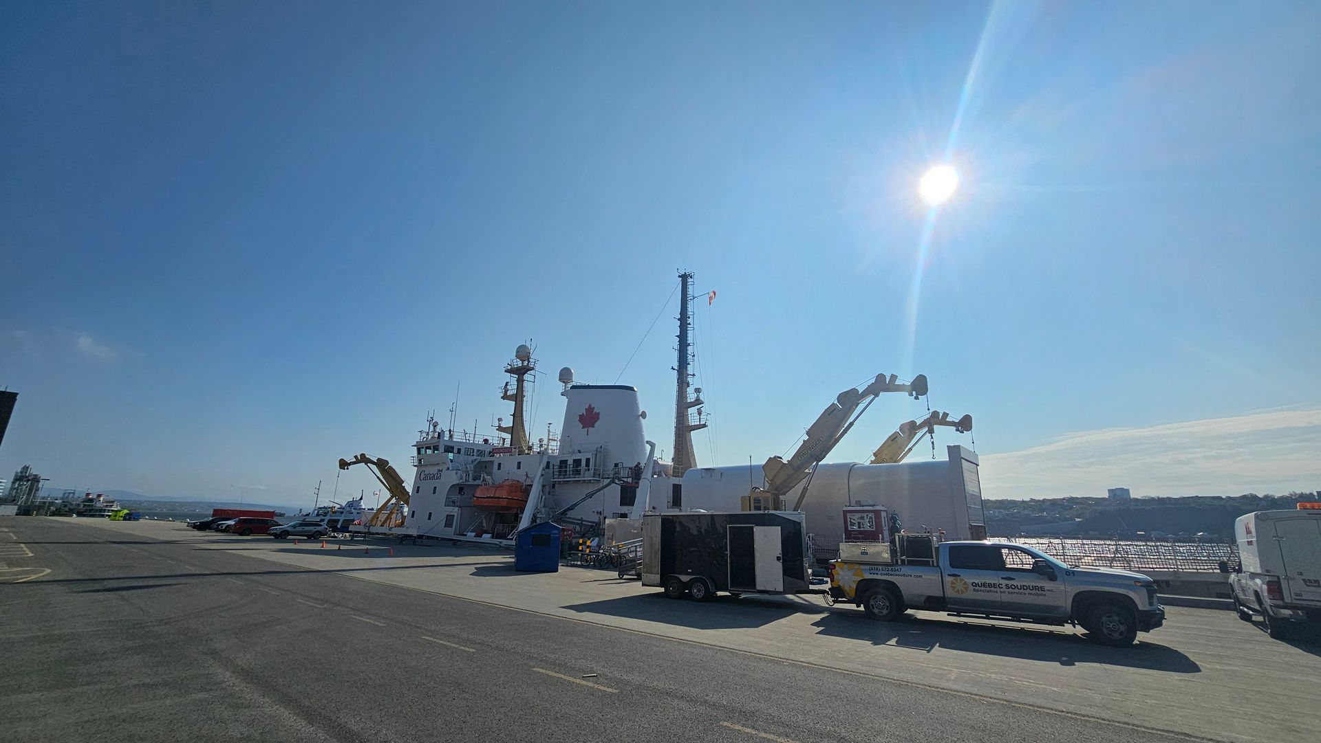 Un navire des garde-côtes canadiens a accosté dans un port pavé sous un soleil radieux, avec des engins de chantier à proximité.