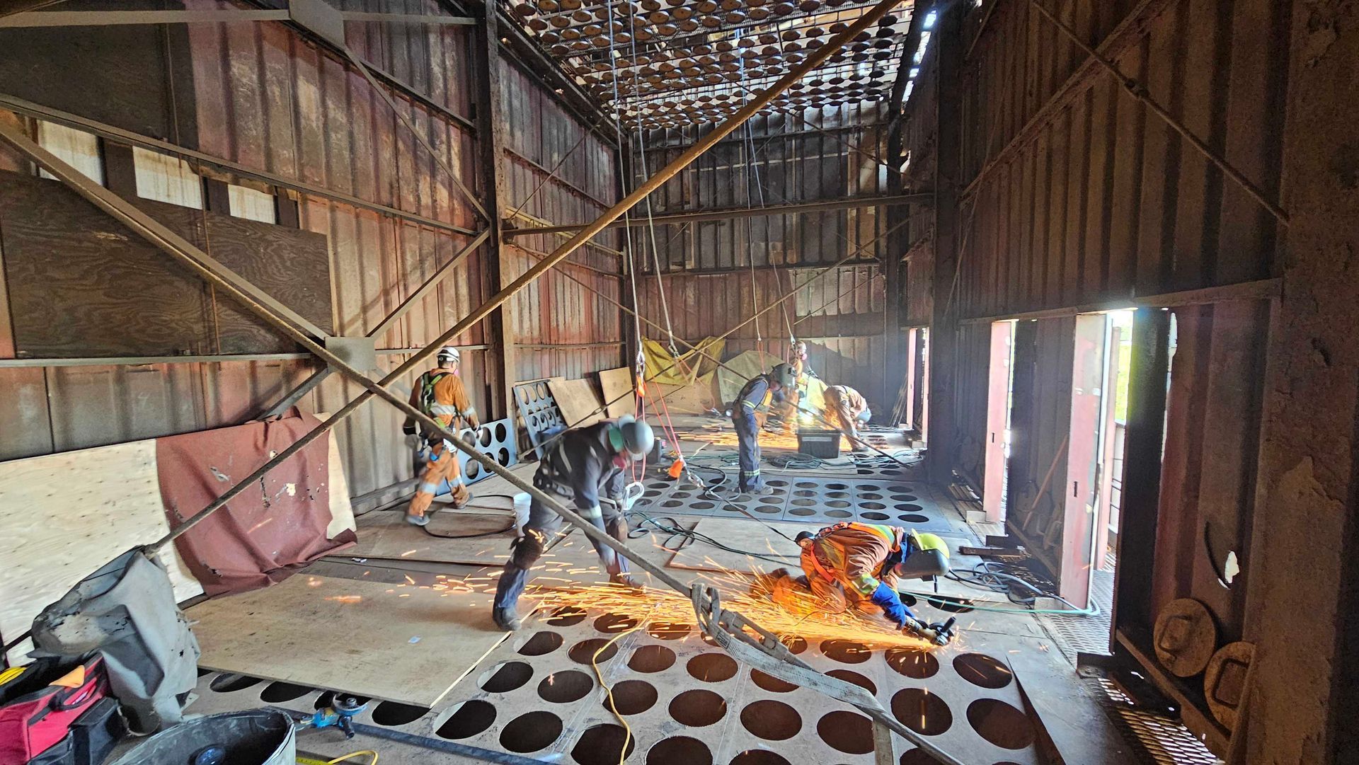 Des ouvriers utilisent des chalumeaux pour découper une structure métallique à l'intérieur d'un bâtiment industriel rustique.
