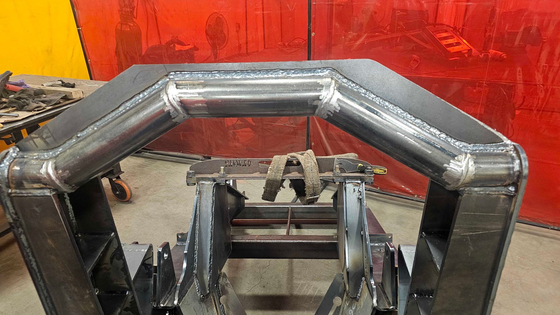 Dans un atelier de soudure, on peut voir un assemblage de cadre en acier sur un support, composé d'une poutre horizontale soudée à deux poteaux verticaux.