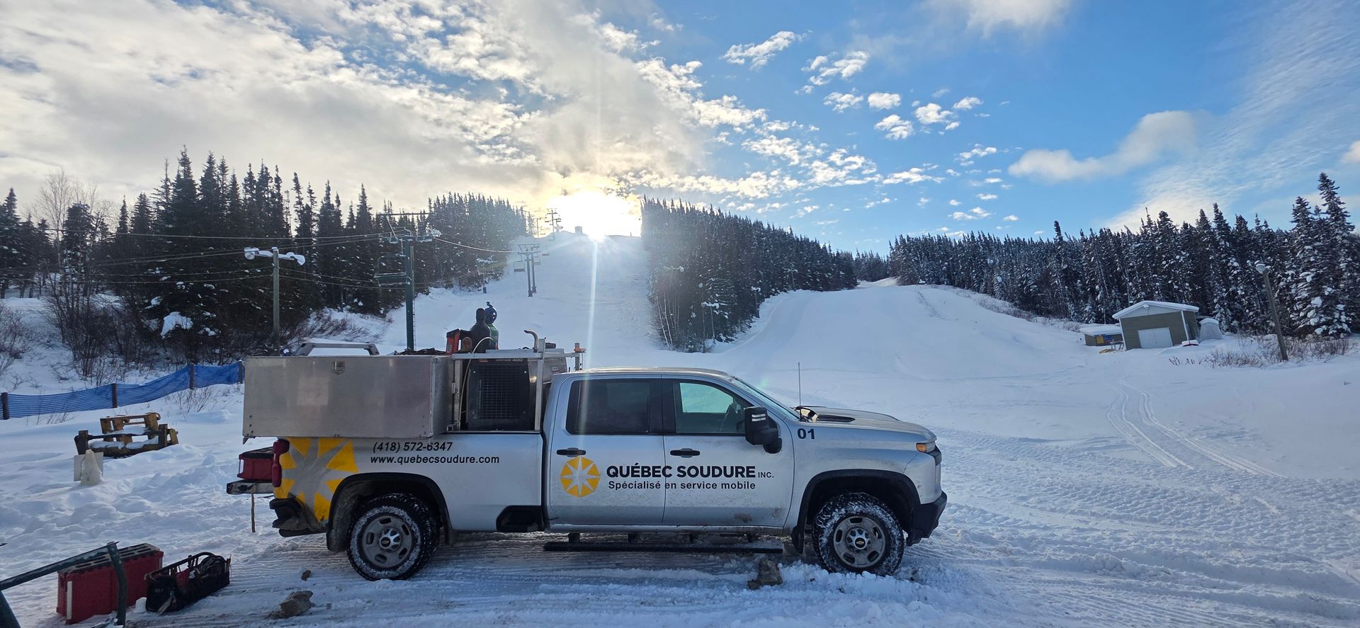 Un camion de service blanc arborant le logo du Mont Washington est stationné sur la neige au pied d'une station de ski, sous un soleil éclatant.