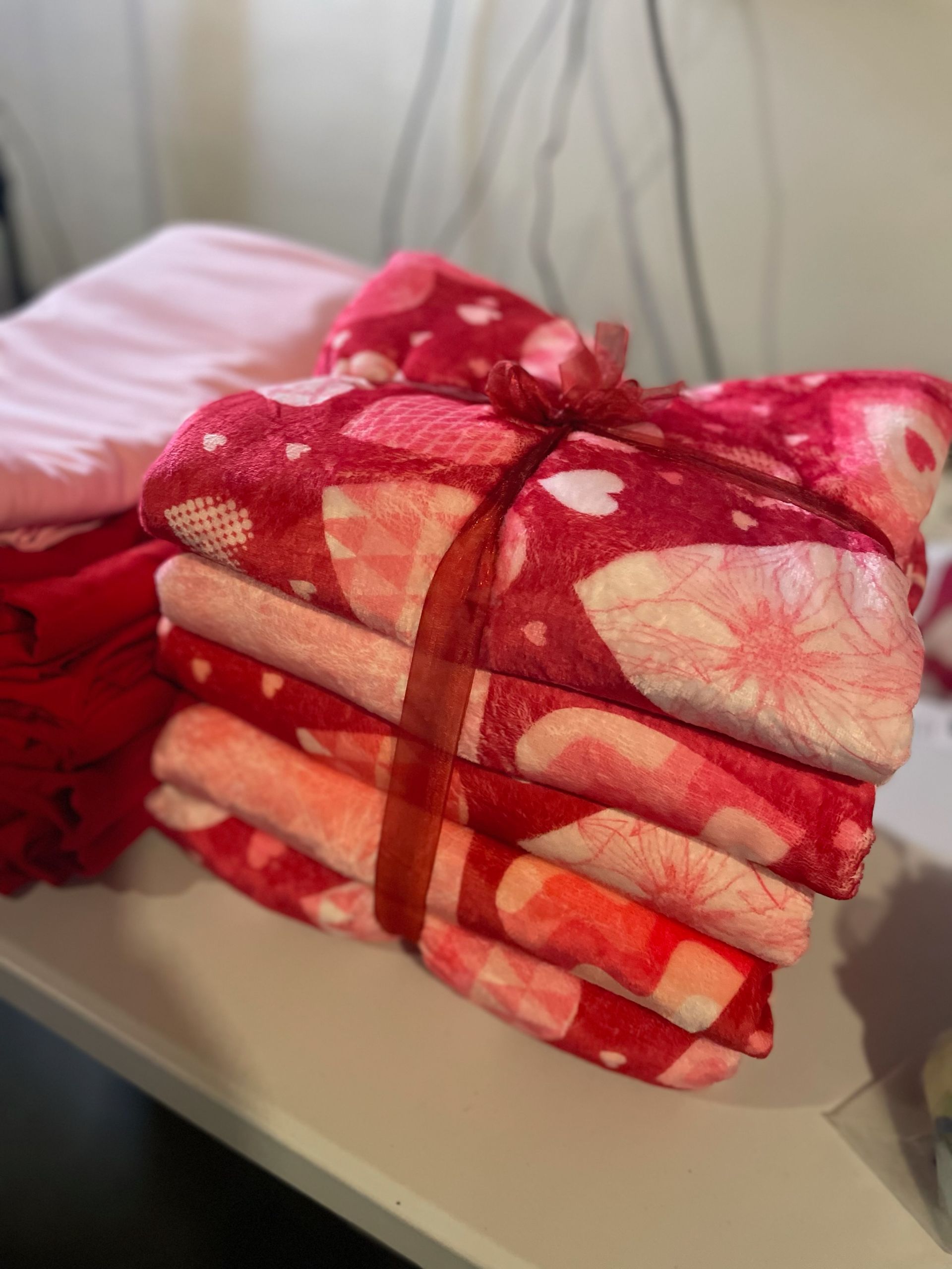 Stacked blankets tied with a ribbon. The blankets are red and pink with a floral print.